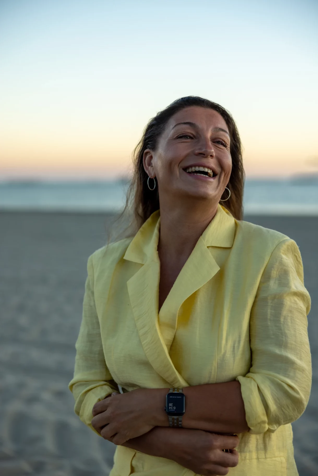 Woman laughing on the beach at sunset in Long Beach, Los Angeles, wearing a yellow jacket