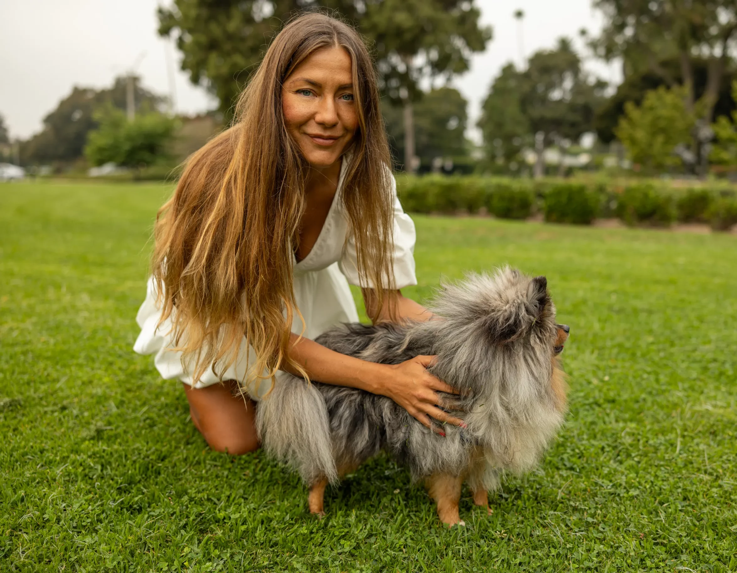 Woman crouching on grass with her Pomeranian in a Beverly Hills park