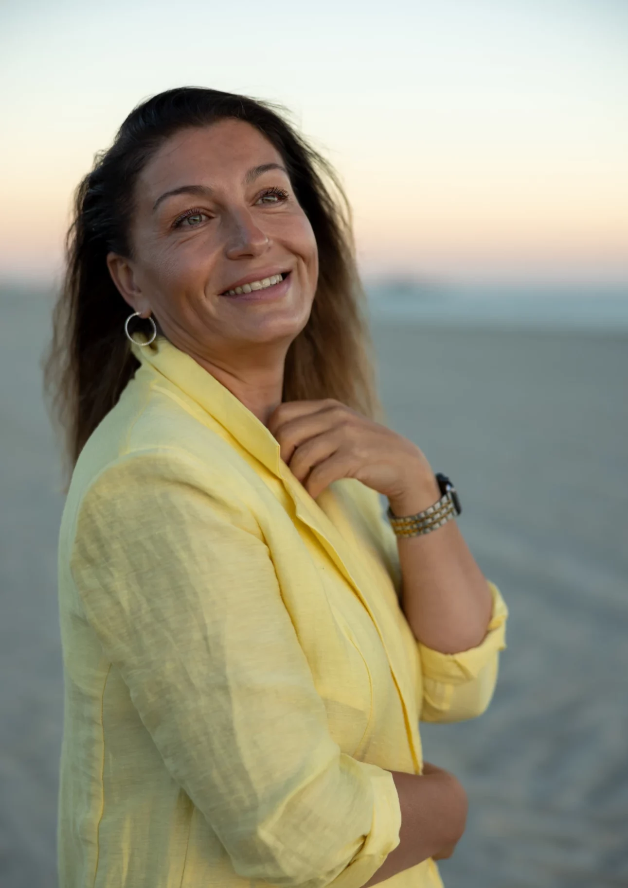 Woman smiling on the beach at sunset in Long Beach, Los Angeles, wearing a yellow jacket
