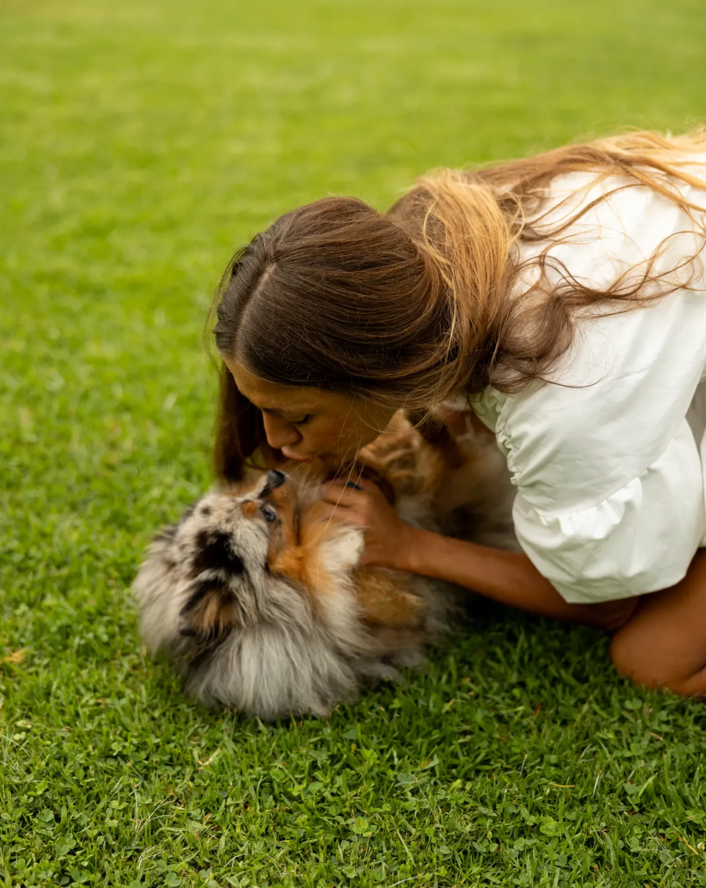 Woman kissing her Pomeranian while lying on grass in Beverly Hills park