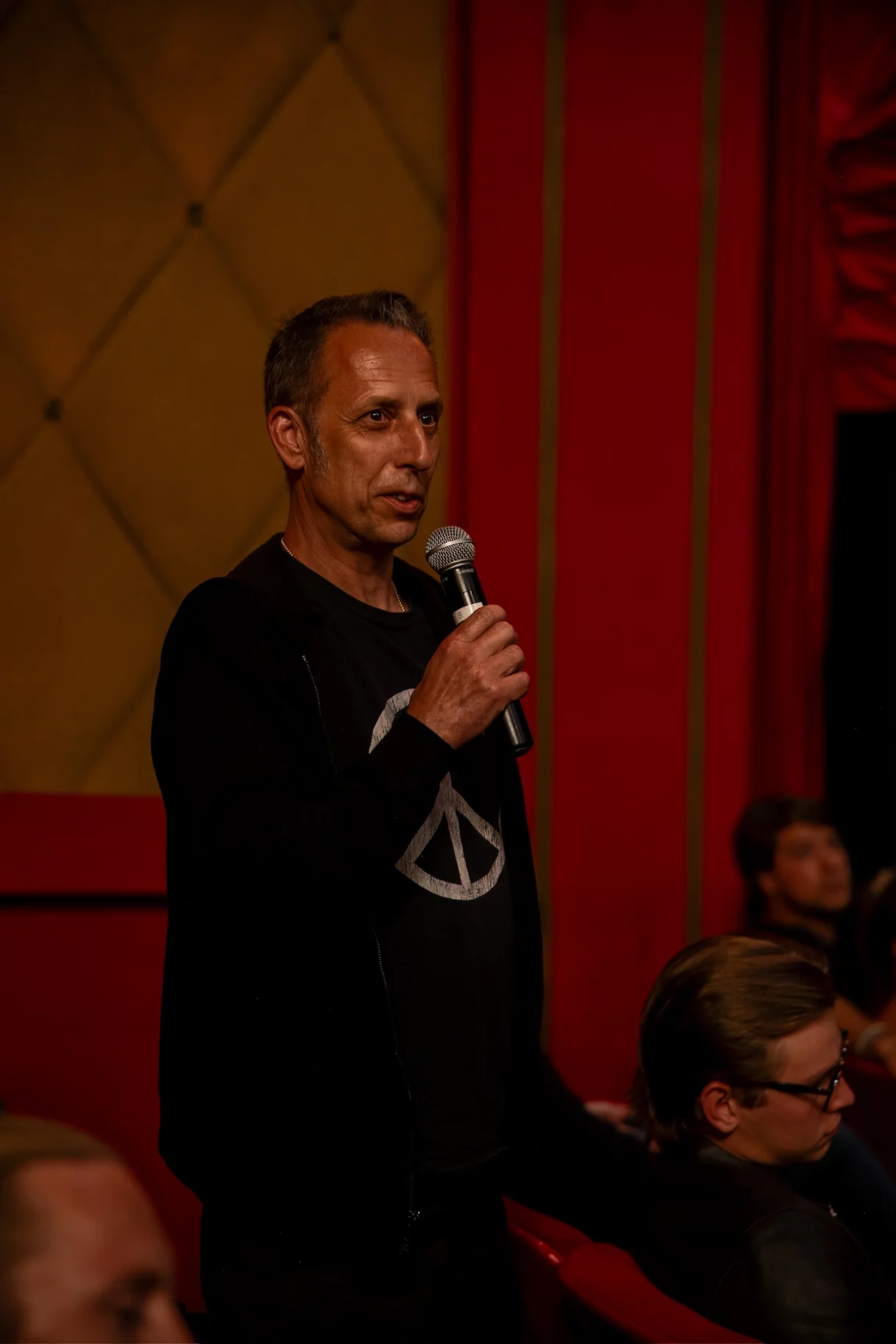 Guest standing in theater aisle with microphone, directly engaging with speakers by asking questions during an event at the Fine Arts Theater in Beverly Hills.