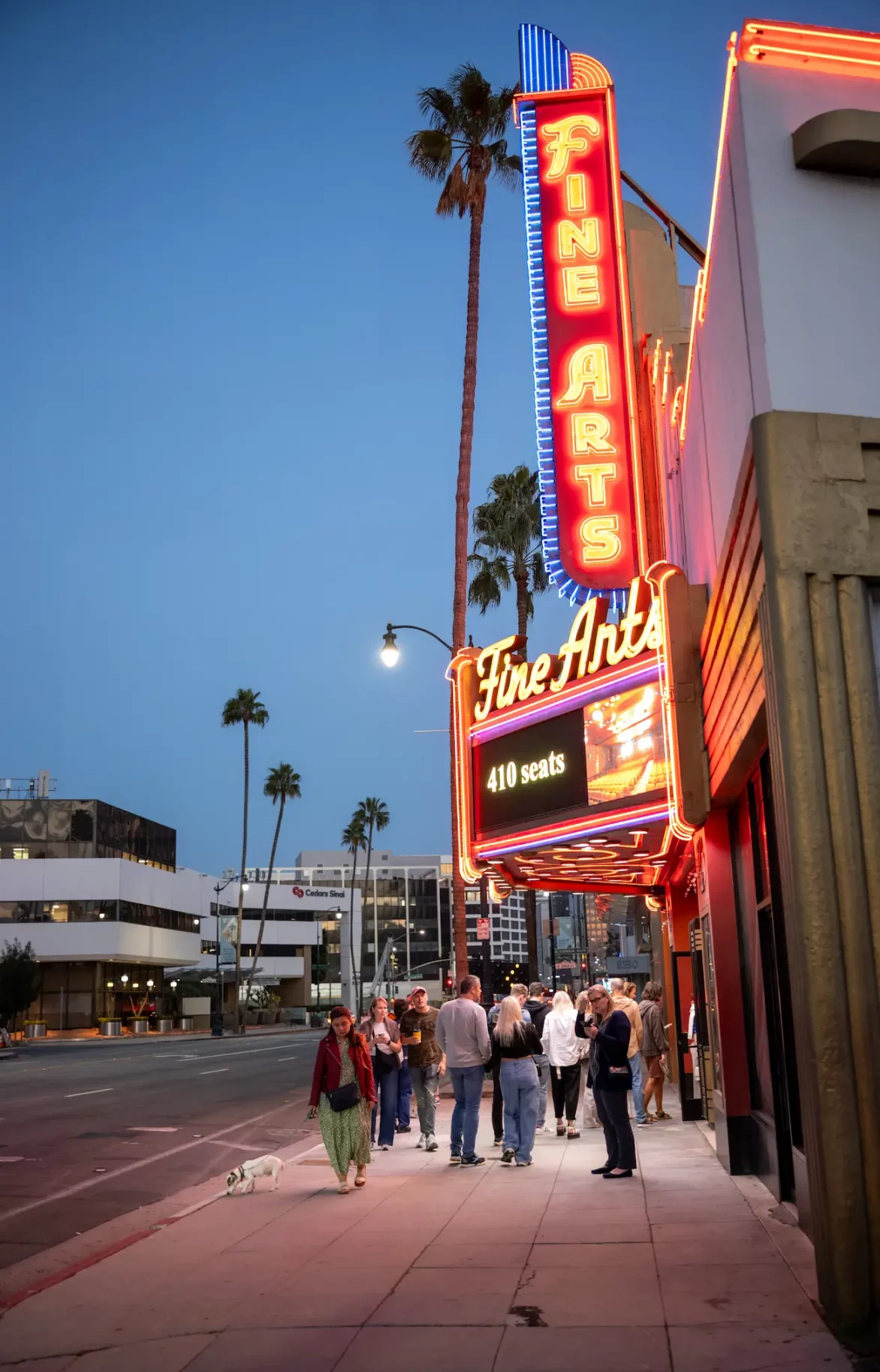 Fine Arts Theater in Beverly Hills, Los Angeles, evening scene with illuminated neon sign and people gathered outside. The sidewalk view showcases the theater’s iconic look and the vibrant city atmosphere