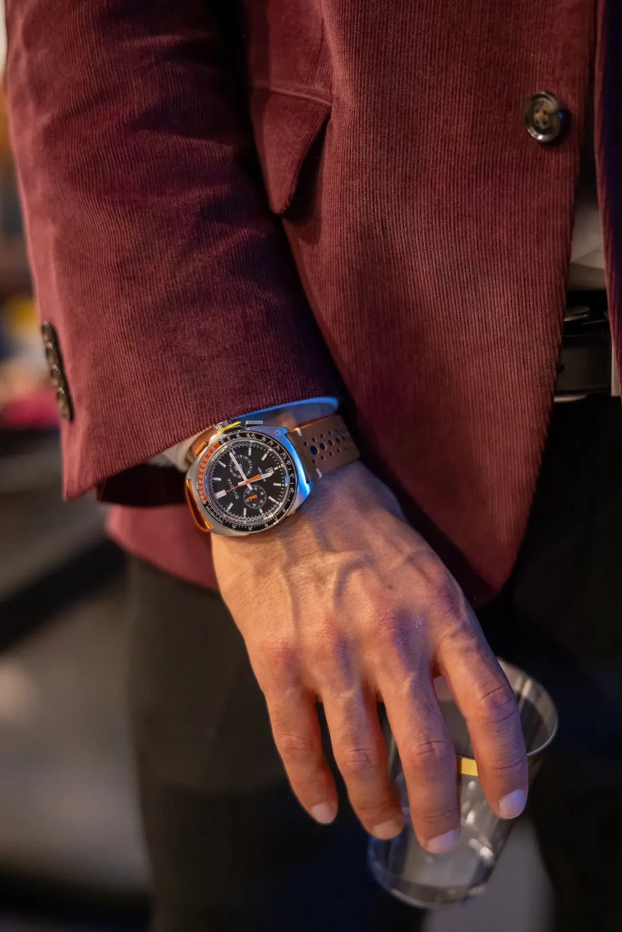 Close-up of a man’s hand wearing a luxury wristwatch, holding a drink.