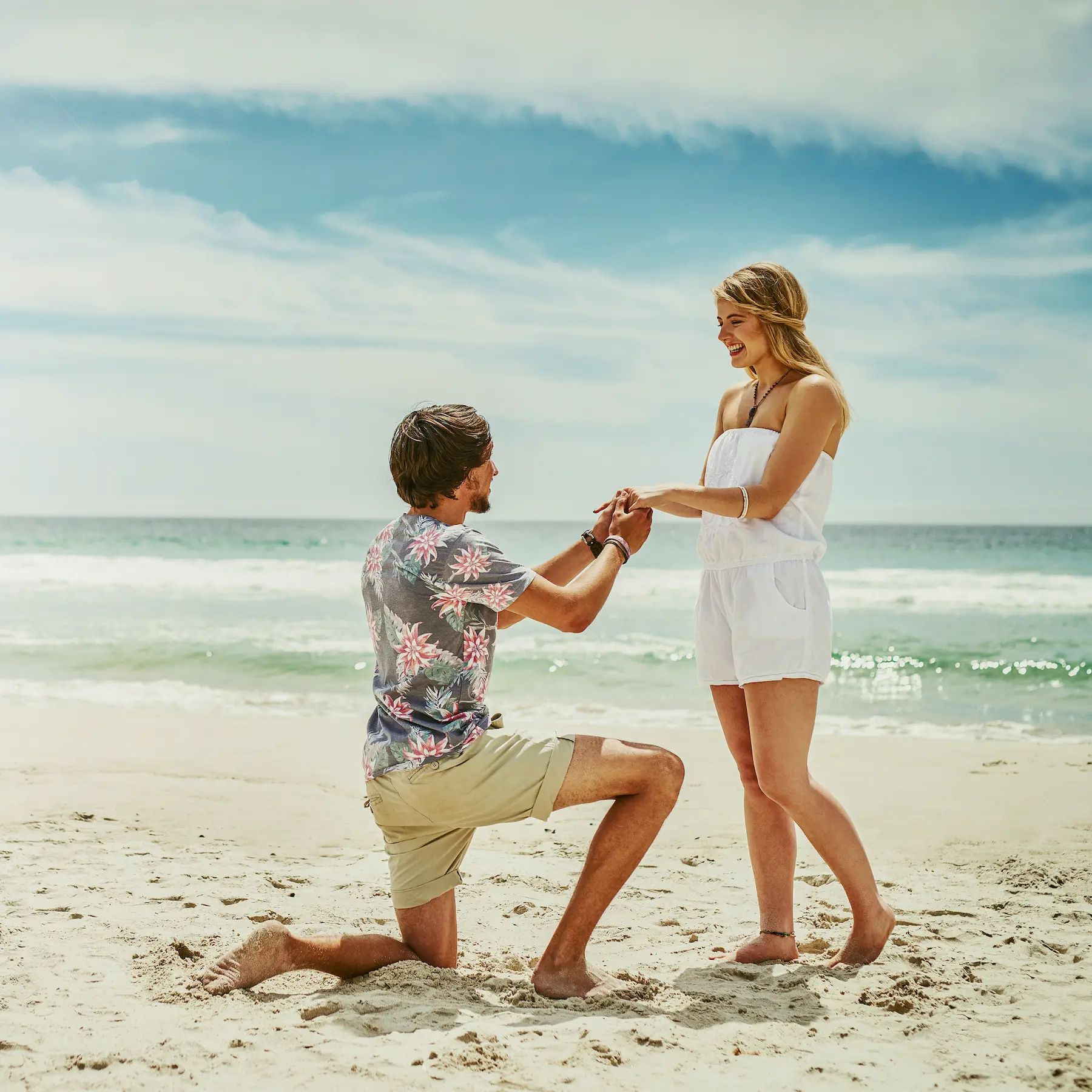 Una romántica propuesta de matrimonio en la playa de Long Beach, Los Ángeles: un hombre arrodillado le ofrece un anillo a su pareja bajo un cielo luminoso.