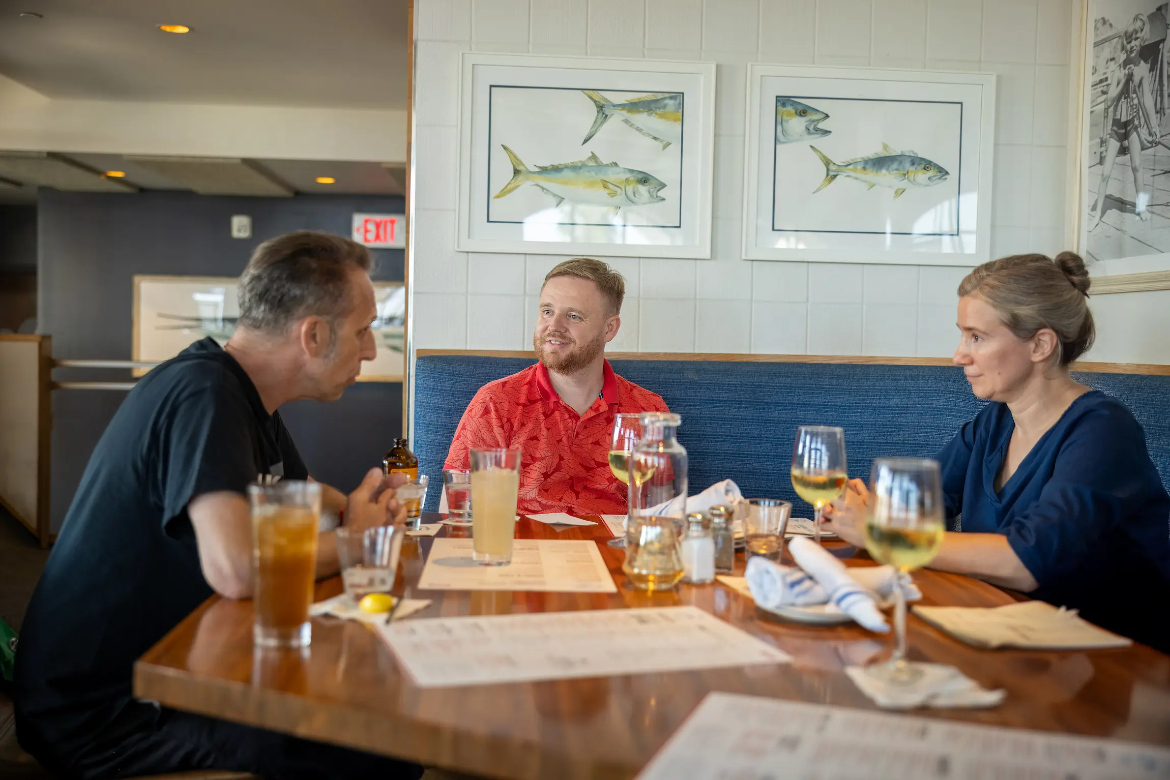 Un grupo de tres personas disfruta de una comida informal en un restaurante con cuadros de peces en la pared.