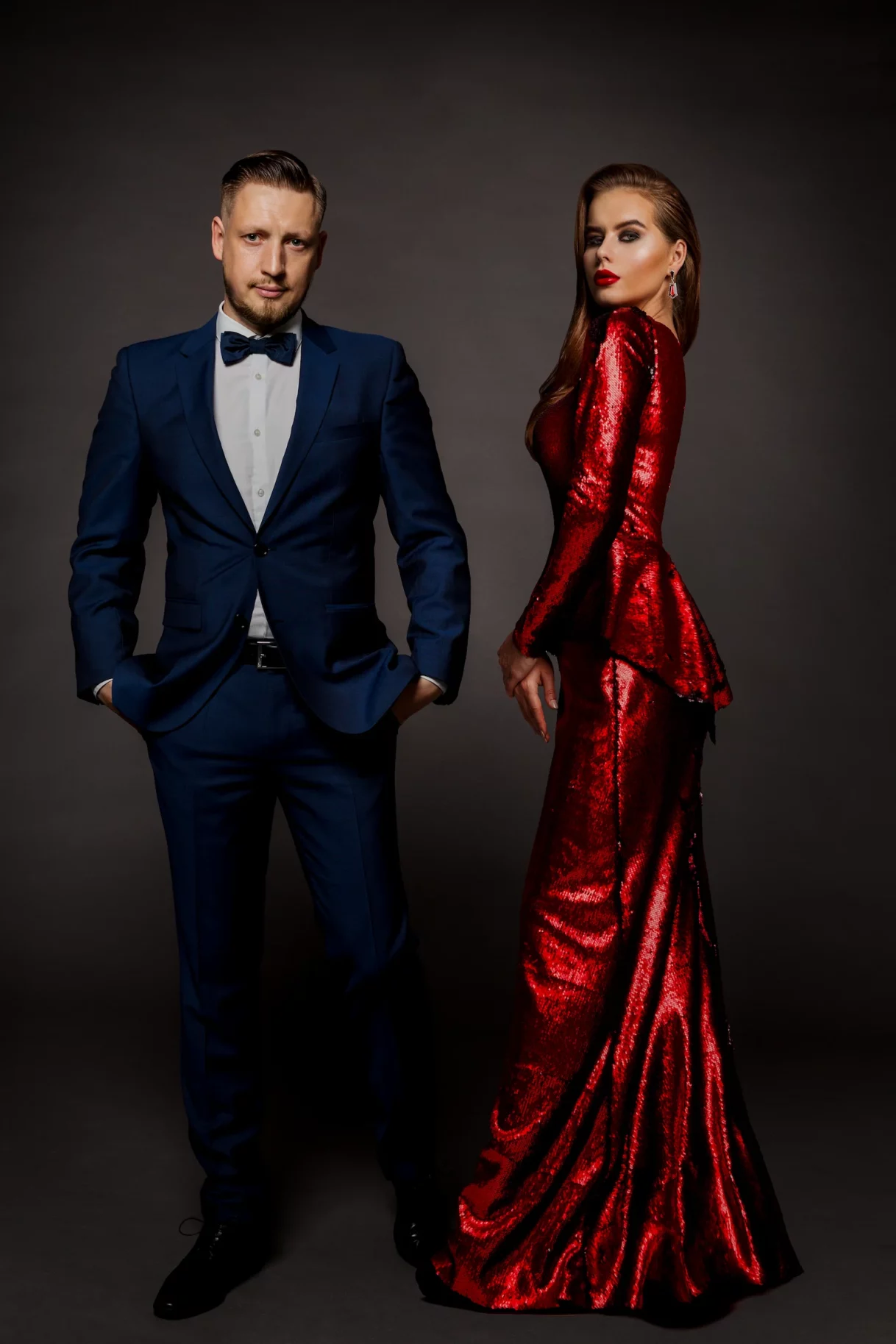 Una pareja elegante posando junta: él con un impecable traje azul y moño, y ella con un glamoroso vestido rojo de lentejuelas — MayerPix Photography