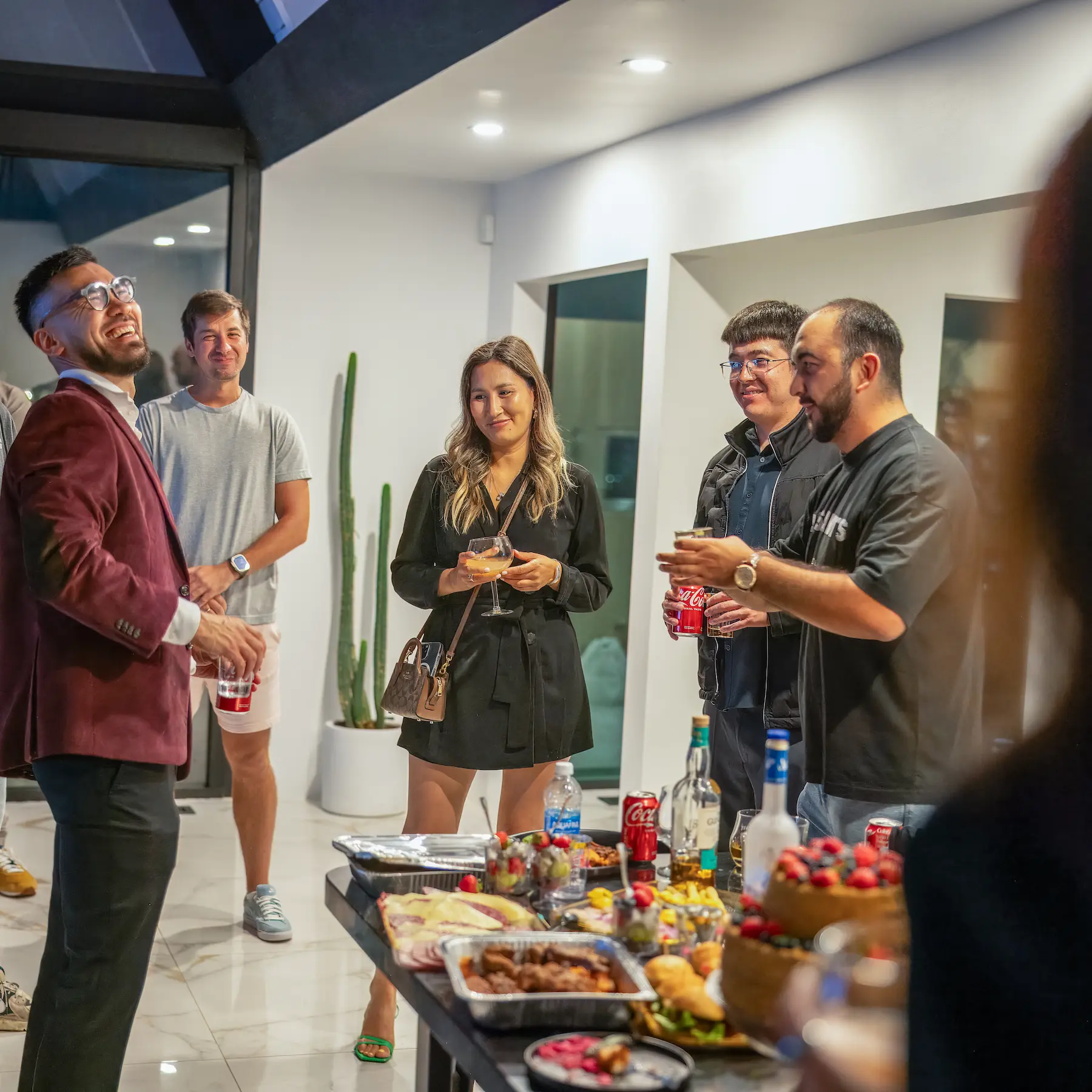 Invitados disfrutando de una animada fiesta nocturna con comida y bebidas en un espacio moderno