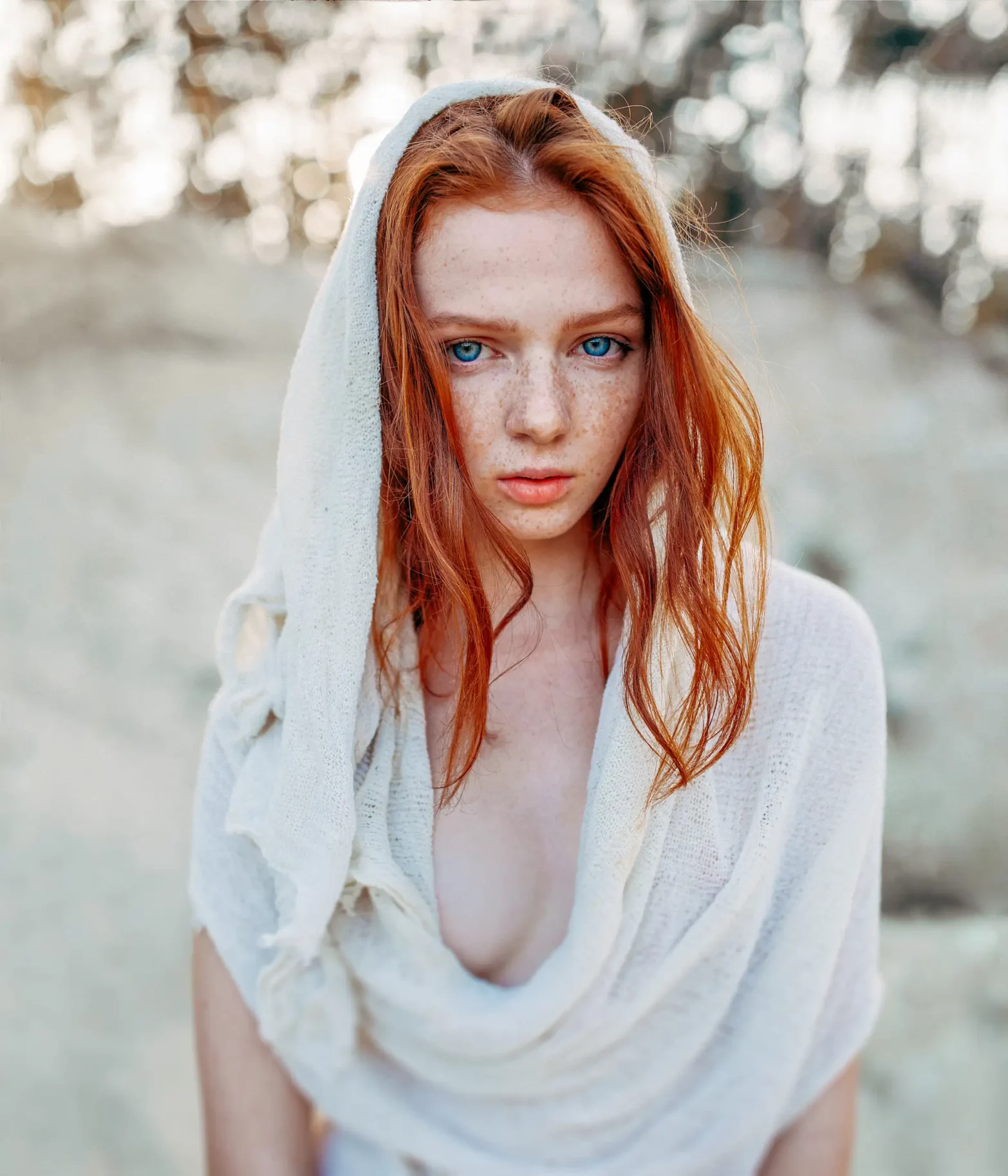 Retrato con luz natural de una mujer pelirroja con pecas y un chal blanco, al aire libre.
